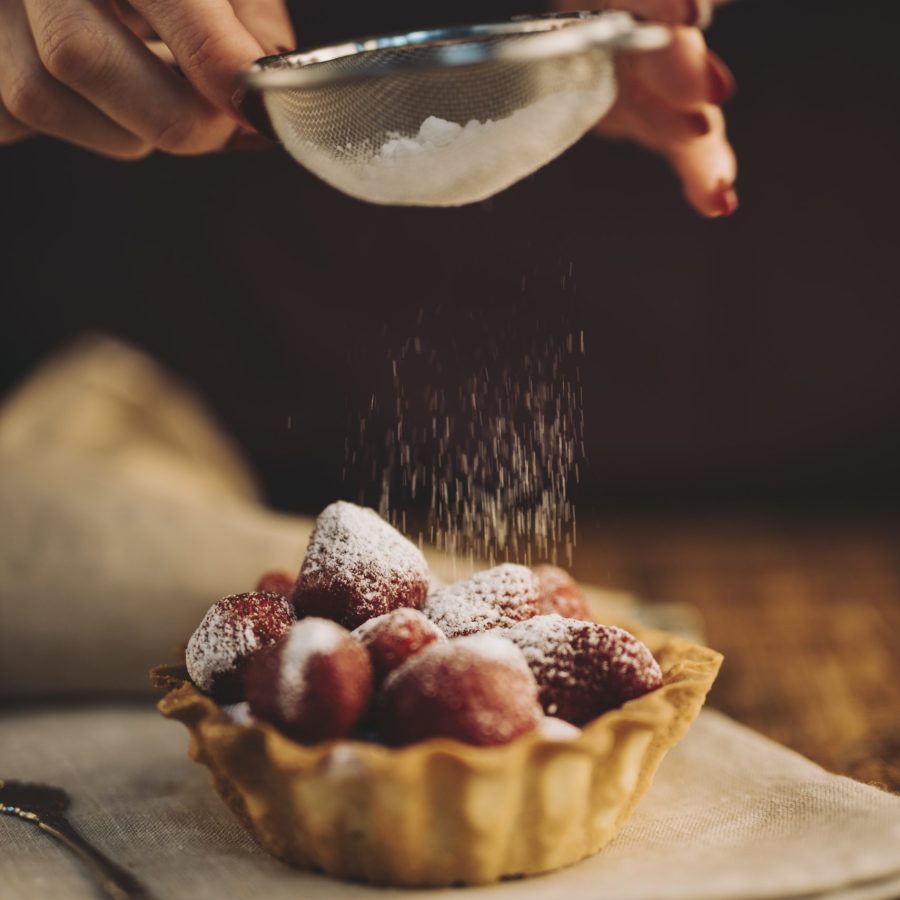 close-up-woman-dusting-sugar-powder-strawberry-tart